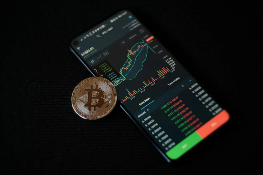 A mobile showing the graphics of Bitcoin trading and a bitcoin placing aside of mobile.