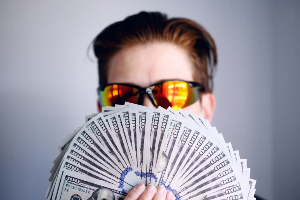 A man wearing sun glasses covered his face with dollar notes